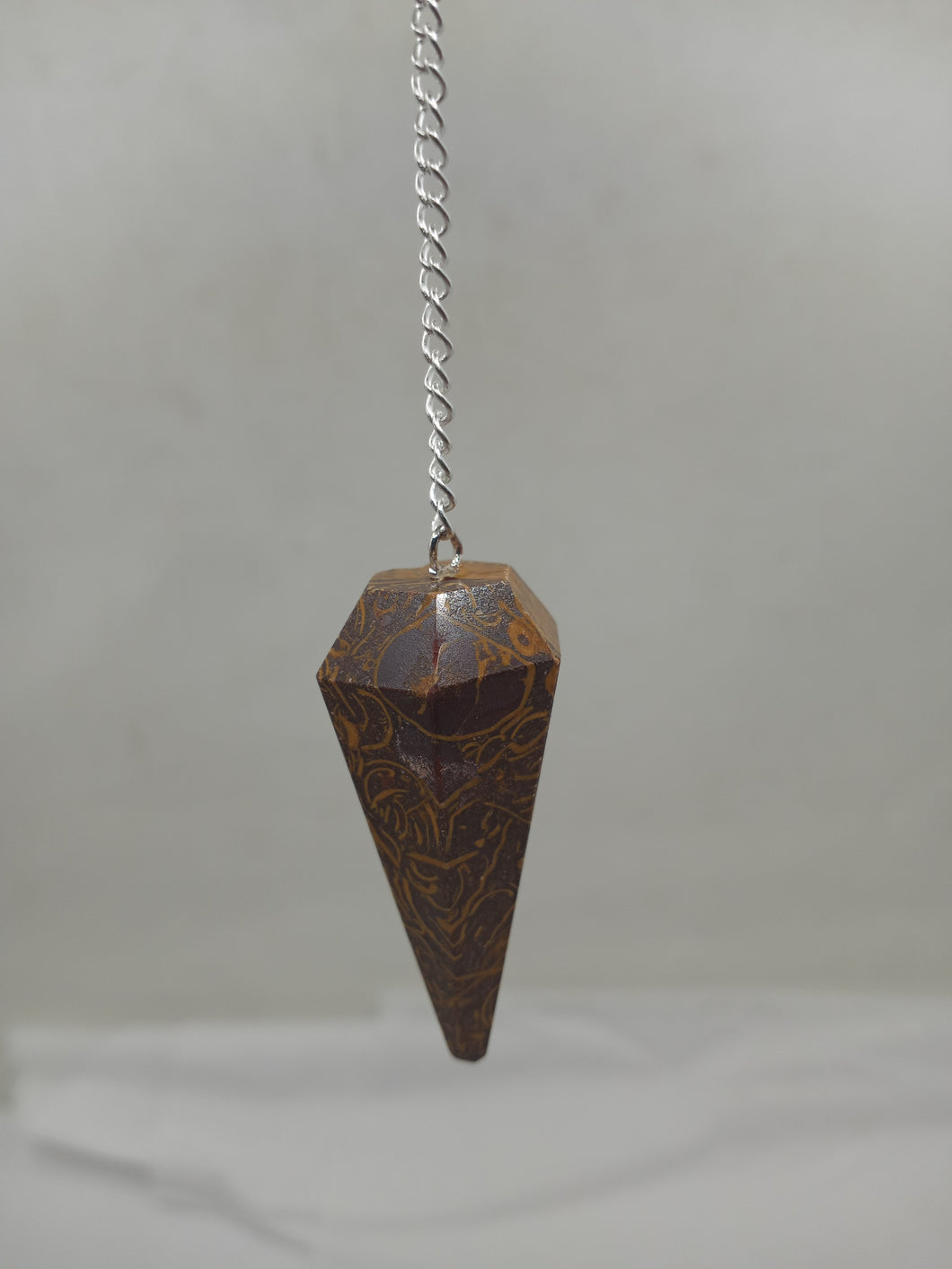 A beautiful brown Miriam stone pendulum elegantly hangs from a silver chain.