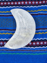 Load image into Gallery viewer, A Selenite Bowl Crescent Moon Shaped holds white quartz stone on blue and white striped cloth.
