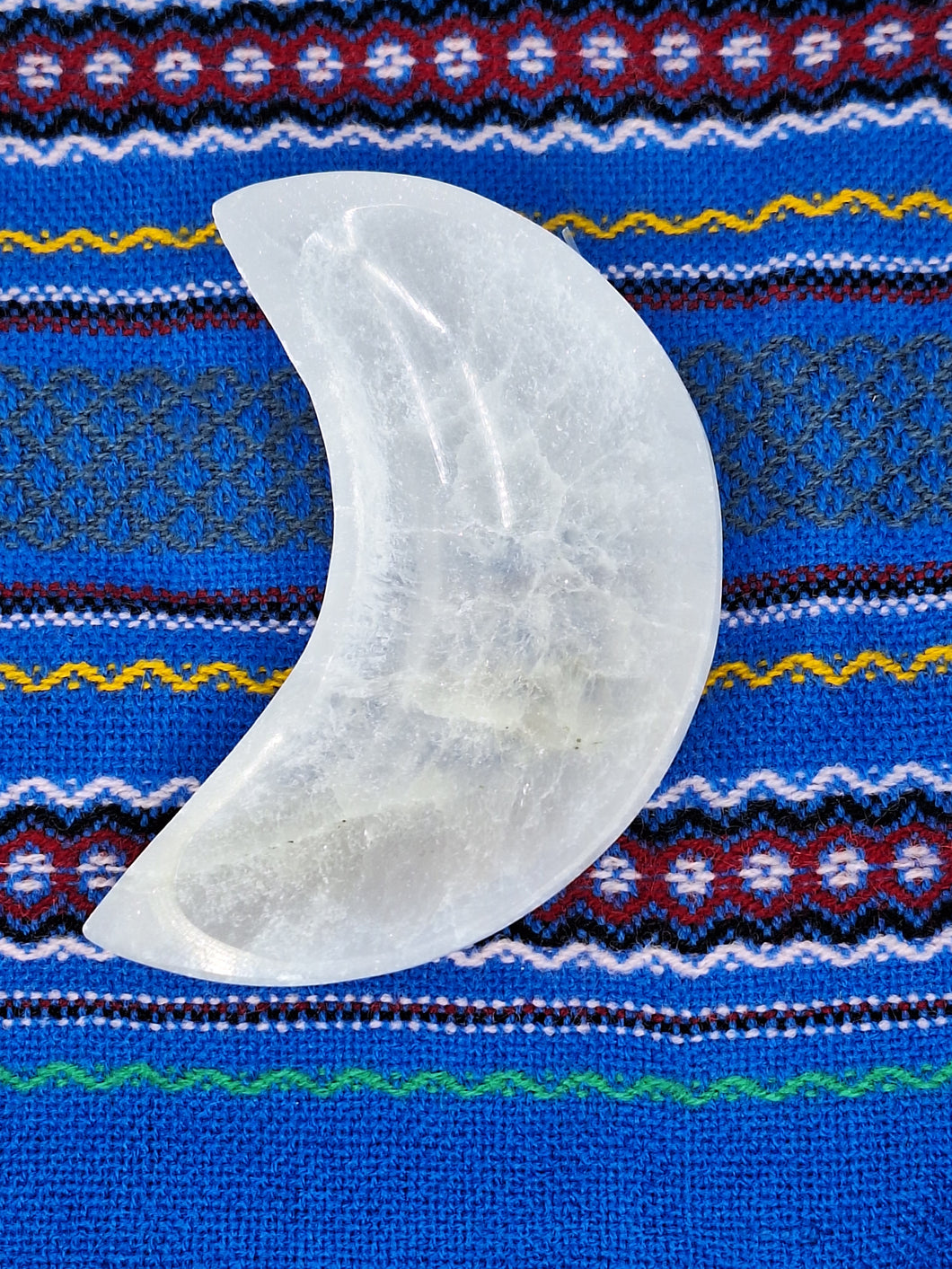 A Selenite Bowl Crescent Moon Shaped holds white quartz stone on blue and white striped cloth.