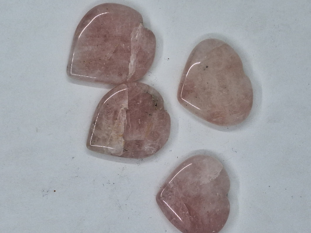 A set of 4 rose quartz heart worry stones on a white background.
