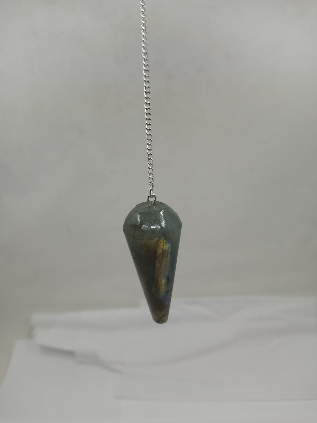 A beautiful labradorite rounded pendulum elegantly hangs from a silver chain on a serene white background.