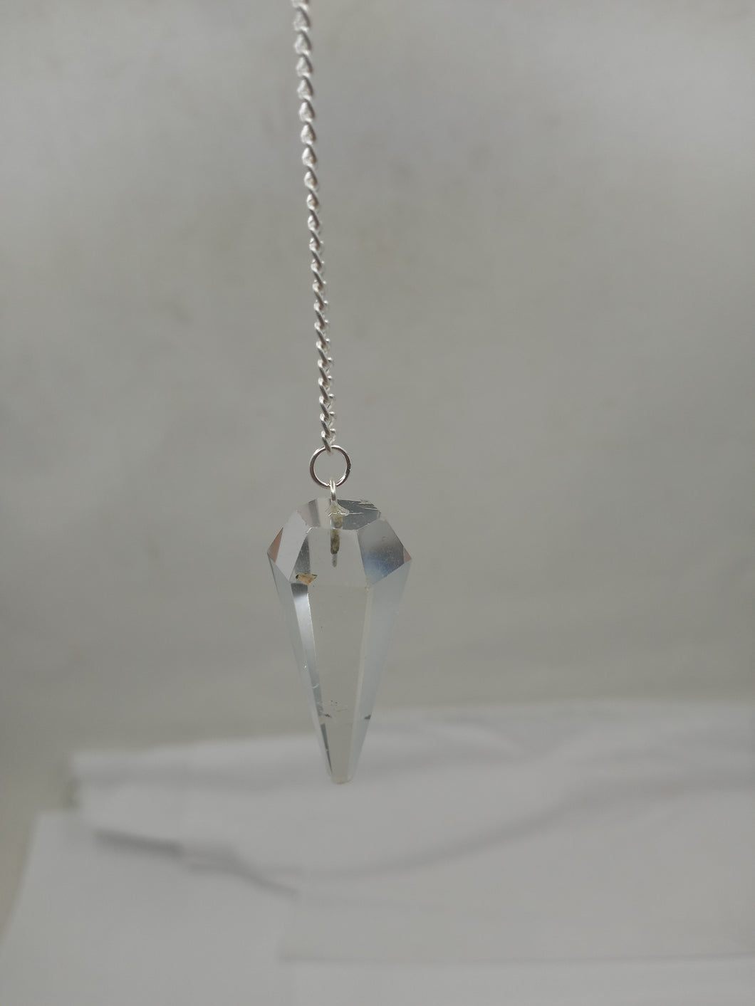 A beautiful clear quartz pendulum with a faceted point. The pendulum hangs from a silver chain with a small clasp at the top.