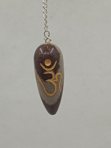 A beautiful Narmada lingam-shaped om-engraved pendulum elegantly hangs from a silver chain.