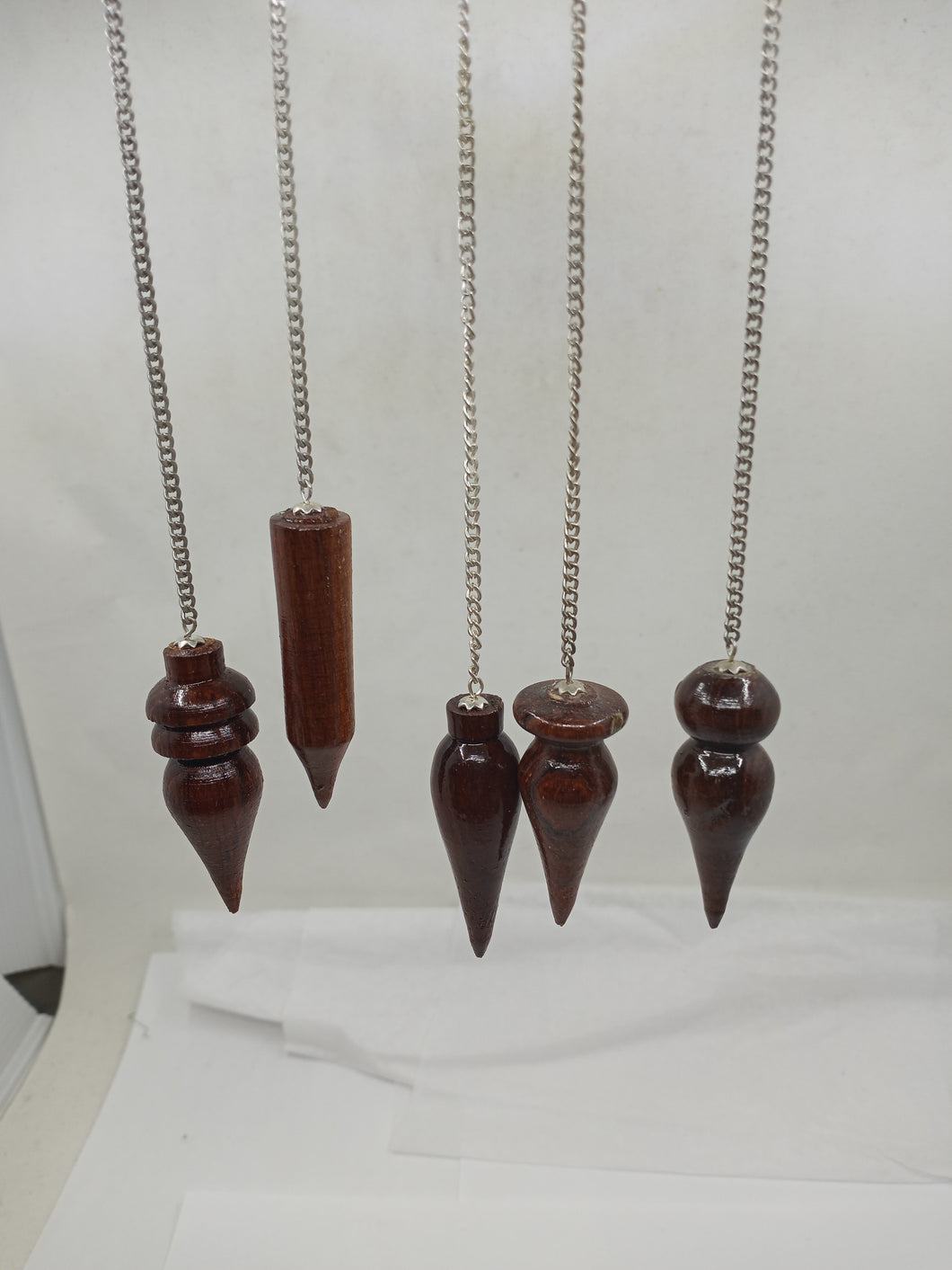 A collection of exquisite rosewood pendulums, each uniquely shaped, elegantly hangs from a silver chain.
