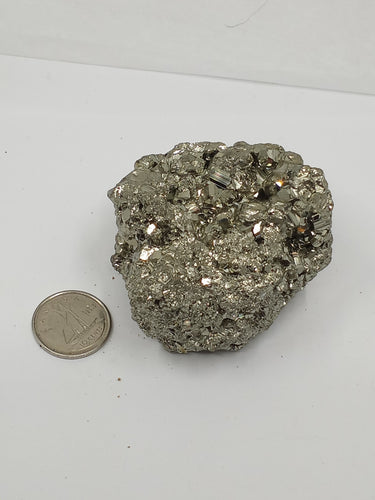 A natural pyrite cluster silver crystal with a coin on the serene white surface.