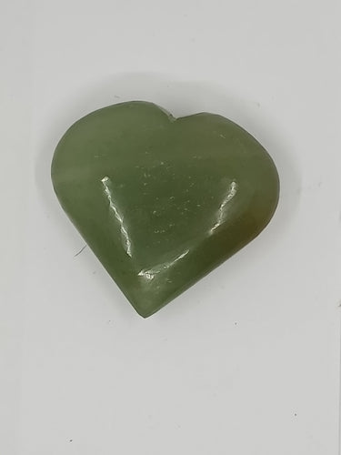 A green heart-shaped aventurine puffy heart stone resting on a white surface.