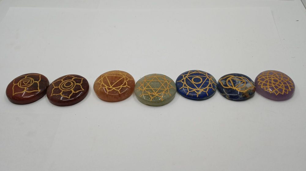 A set of seven disc-shaped chakra stones in a row with different colors and reiki symbols engraved on its surface.