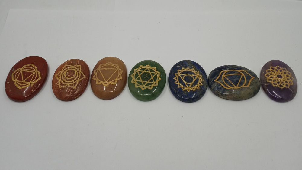 A set of seven, oval-shaped chakra stones in a row of seven colors with a reiki symbol engraved on its surface.