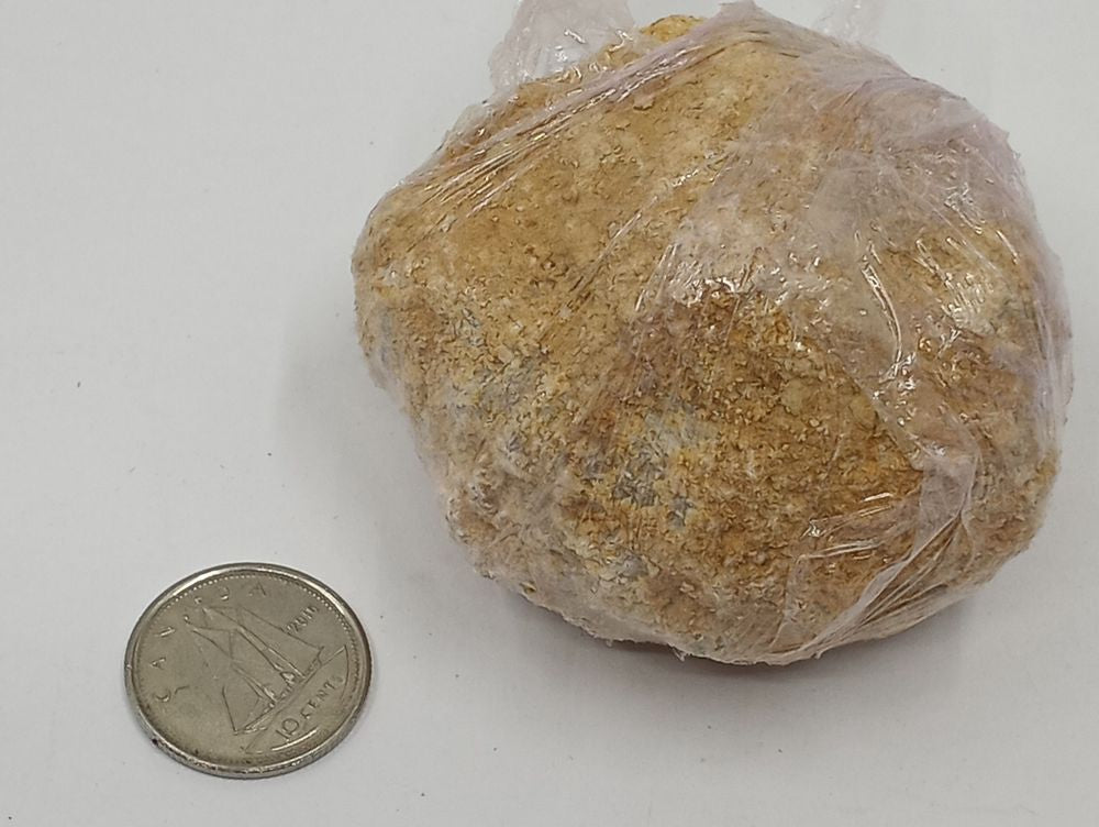 A geode stone wrapped in transparent cellophane with coin on serene white surface.