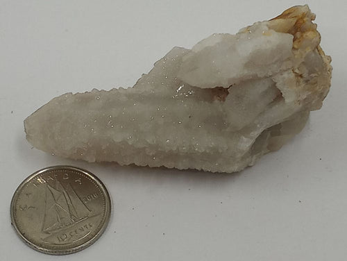 A cluster of clear quartz crystals with pointed ends with a coin on serene white background.