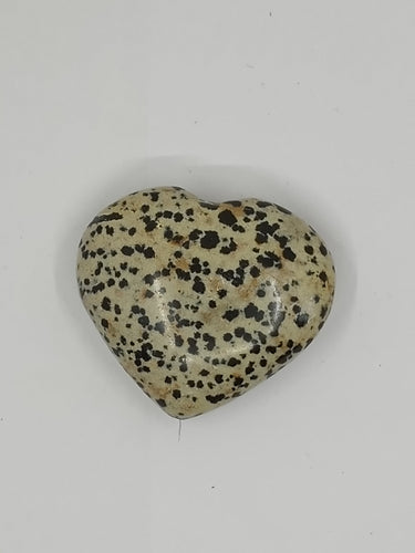 A heart-shaped Dalmation Stone with black and white speckles is placed on a white background.