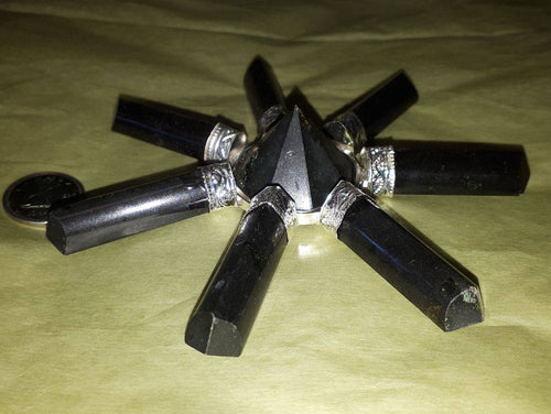 A pyramid made of multiple pointed black tourmaline crystals with a coin.