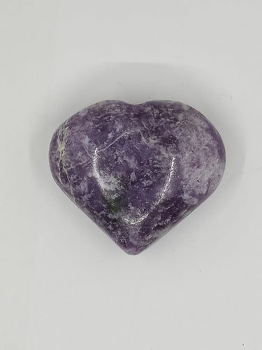 A purple lepidolite puffy heart stone resting on a white surface.