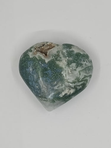 The green agate moss puffy heart stone on a plain white surface.