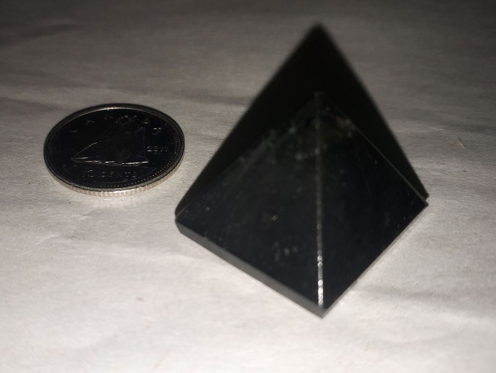 A black tourmaline pyramid 18-20mm stone with a silver coin on a white background.