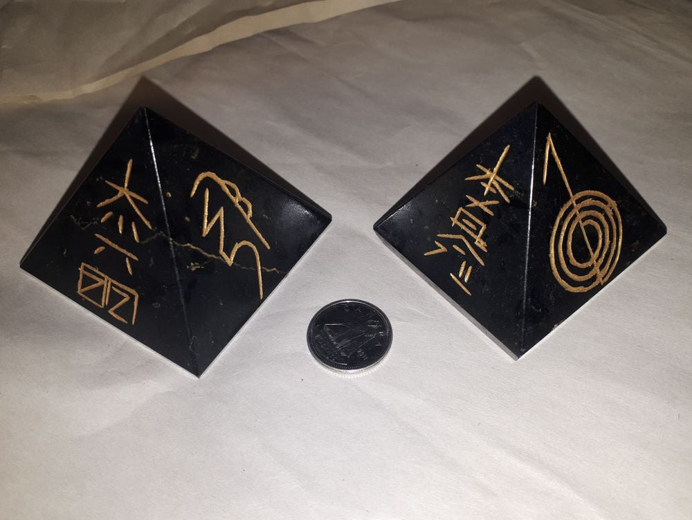 A beautiful two-black obsidian pyramid engraved with reiki sign stone with a silver coin on a serene white background.
