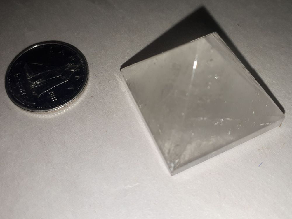 A beautiful clear quartz pyramid of 18-20mm stone with a silver coin on a serene white background.