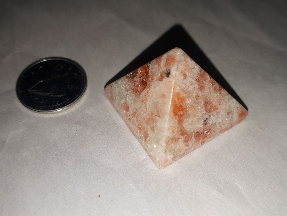 A beautiful sunstone pyramid of 18-20mm stone with a silver coin on a serene white background.