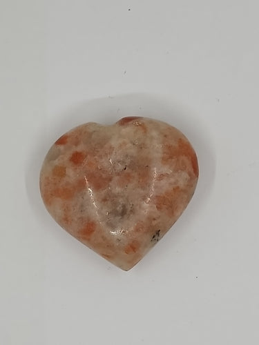 A puffy heart-shaped sunstone with speckles of orange and white.