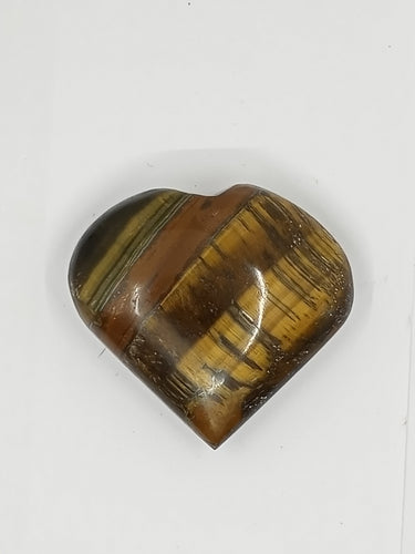 A heart-shaped tiger eye stone with brown and black stripes on a white surface.